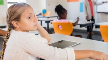 一个小女孩坐在教室里，背对着老师。
